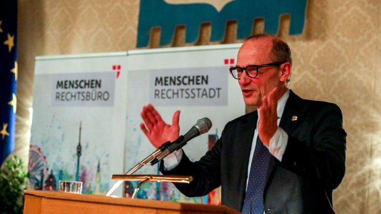 copyright: Stadt Wien/Christian Fürthner Ein Mann mit schwarzer Brille und schwarzem Sakko spricht in ein Mikrofon am Rednerpult.