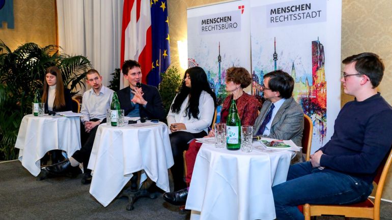 copyright: Stadt Wien/Christian Fürthner Mehre Menschen an kleinen runden Tischen, ein Mann spricht in ein Mikrofon.