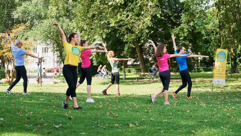 6 Menschen in bunten Shirts bei Turnübungen im Park