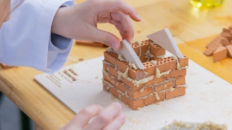 Hand eines Mädchens baut ein Miniaturhaus aus kleinen Ziegeln