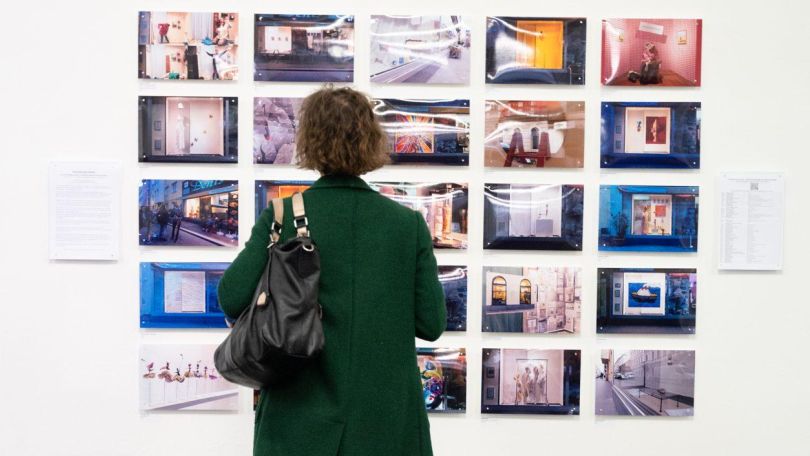 Eine Frau betrachtet Fotografien an einer Wand.