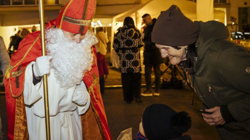 Nikolaus übergibt Kind ein Geschenk. Daneben steht eine lächelnde Frau.