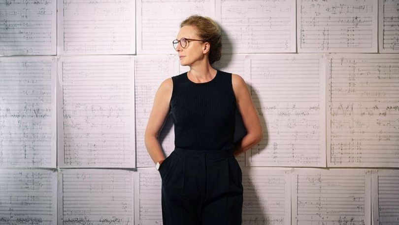 Rebecca Saunders lehnt an einer Wand, die mit Notenblättern tapeziert ist