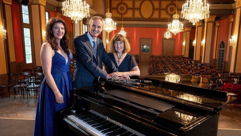 copyright: Dominik Frühauf House of Strauss Die 3 Musiker*innen des Trios Clarivoce stehen um einen Konzertflügel in einem Konzertsaal