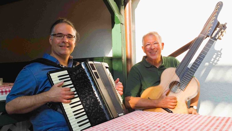 2 Musiker am Tisch sitzend, einer mit Akkordeon und der andere mit Gitarre