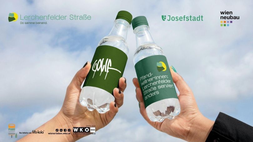 copyright: IG Kaufleute Lerchenfelder Straße Zwei Hände, die zwei Pfandflaschen in die Luft halten. Das Foto ist von unten aufgenommen, sodass man im Hintergrund den blauen Himmel erkennen kann. Auf der linken Pfandflasche ist die Wortmarke des Künstlers GOLIF platziert, auf der rechten Pfandflasche liest man "Pfandkellner*innen: Lerchenfelder Straße serviert anders"