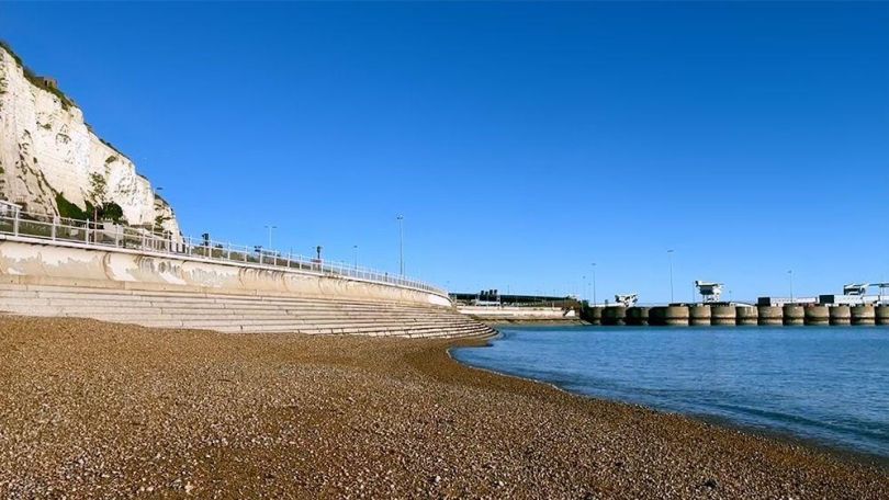 copyright: Aria Danaparamita Seeküste mit Kieselstrand, links ist ein Teil eines Berges sowie eine Straße zu sehen. Heller, blauer Himmel.