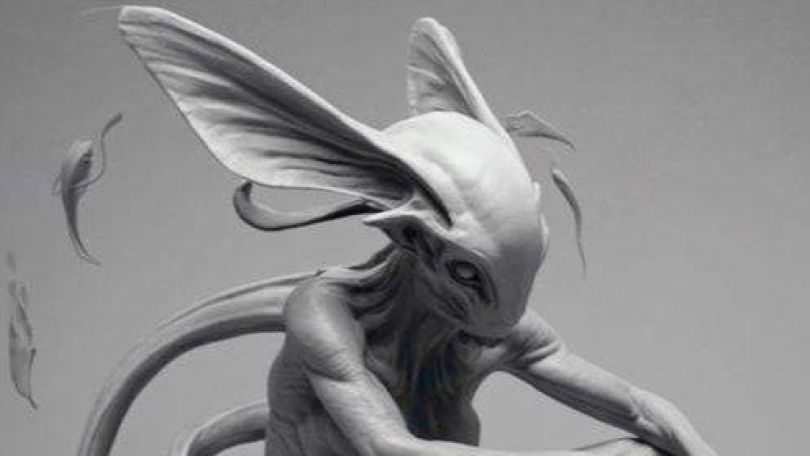 copyright: Tanja Vujinovic Eine nicht-menschliche Figur ohne Haare mit langen nach oben stehenden Ohren, großen Augen, ohne Nase und langem Schwanz sitzt mit verschränkten Armen in der Hocke.