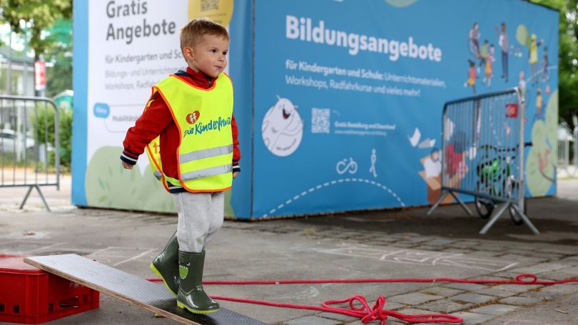 Ein Bub in gelber Warnweste balanciert über ein Brett.