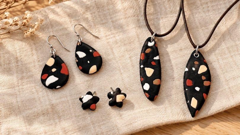 copyright: Sunnyside by Moni Ohrringe und Kettenanhänger aus schwarzem Polymer Clay im Terrazzo-Look mit roten, weißen und cremefarbenen Farbstückchen auf hellem Leinenstoff