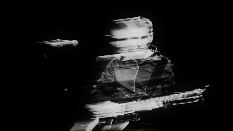 copyright: Hanna Fasching Schwarz-Weiß-Aufnahme einer Person mit E-Gitarre auf einer dunklen Bühne, dargestellt mit Bewegungsunschärfe und Lichtspuren.