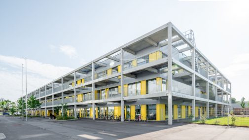 zweigeschoßiges Gebäude in den Farben grau und gelb mit Fahrradabstellplätzen