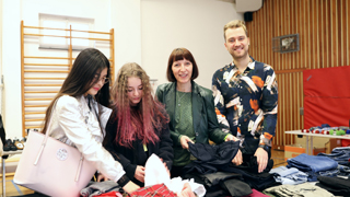 2 Schülerinnen, ein Lehrer und die Direktorin der Modeschule bei einem Tisch mit Kleidung
