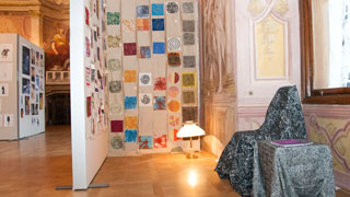 Ausstellungsraum mit Sessel, Lampe und Wand voller bedruckter Textilien mit Formen und Mustern