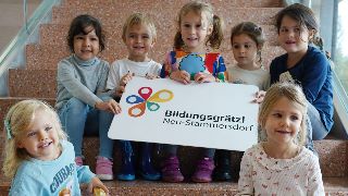 7 Kinder sitzen auf einer Stiege und halten ein Plakat mit der Aufschrift "Bildungsgrtzl Neu-Stammersdorf"