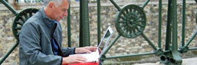 Mann sitzt im Freien und tippt auf einem Laptop