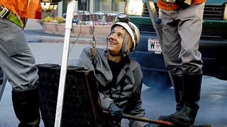 Sewer worker looking out of a manhole, two sewer workers standing to his right and left