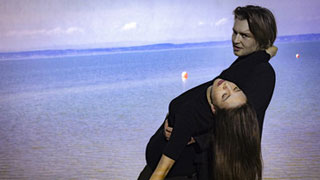 Mann trgt Frau auf den Armen, im Hintergrund Meer  Moritz Schell