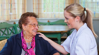 Eine Pflegerin legt einer älteren Dame die Hand auf die Schulter.