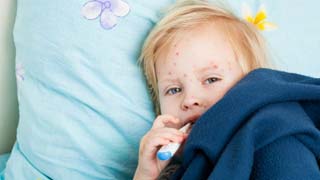 Kind mit Fieberthermometer im Mund unter einer Decke