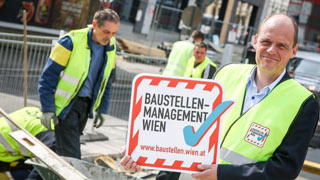 Baustellenkoordinator Peter Lenz prsentiert die neue Baustellenplakette, im Hintergrund Straenbelagsarbeiten