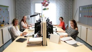 Arbeitssituation: Vier Personen sitzen an Schreibtischen in einem Büro