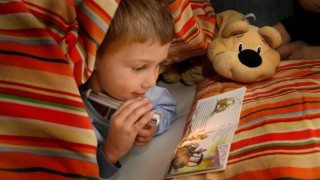 Kind unter der Bettdecke beim Lesen