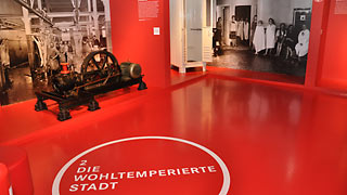 Roter Ausstellungsraum mit Schriftzug "Die wohltemperierte Stadt" am Boden