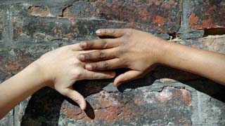 Zwei Kinderhände unterschiedlicher Hautfarbe liegen aufeinander an einer Steinmauer.