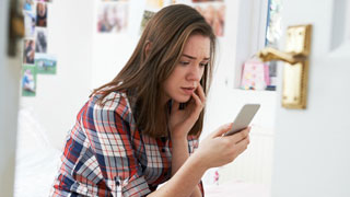 Junge Frau blickt schockiert auf ein Smartphone-Display