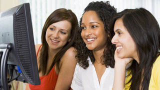 Drei Frauen sitzen lächelnd vor einem Bildschirm.
