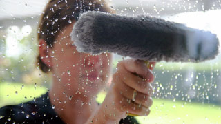 Frau mit Putzutensil hinter einer nassen Glasscheibe