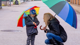 Mutter redet mit Kind und beide halten einen bunten Regenschirm