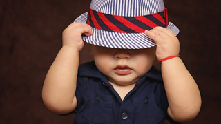 Ein Kleinkind zieht seinen gestreiften Hut tief ins Gesicht, nur Nase und Mund sind sichtbar.
