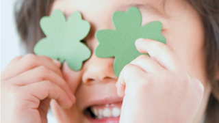Ein Kind hält vierblättrige grüne Kleeblätter vor seine Augen.