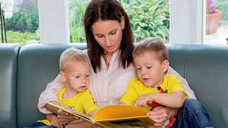 Eine Frau liest zwei Kleinkindern aus einem Buch vor.