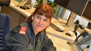 Eine Feuerwehrfrau in einem Kontrollraum mit Telefonen und Monitoren