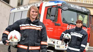 Zwei Feuerwehrfrauen stehen in Montur vor einem Feuerwehrauto