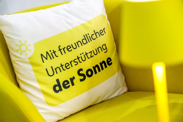 Ein weißes Zierkissen mit der Aufschrift „Mit freundlicher Unterstützung der Sonne“ liegt auf einem gelben Sessel. Copyright: Stadt Wien/Christian Fürthner