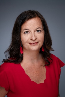 Porträt einer Frau, Stadträtin Ulli Sima, mit dunklem Haar in einem roten Kleid und passenden roten Ohrringen vor grauem Hintergrund. Copyright: Stadt Wien/David Bohmann