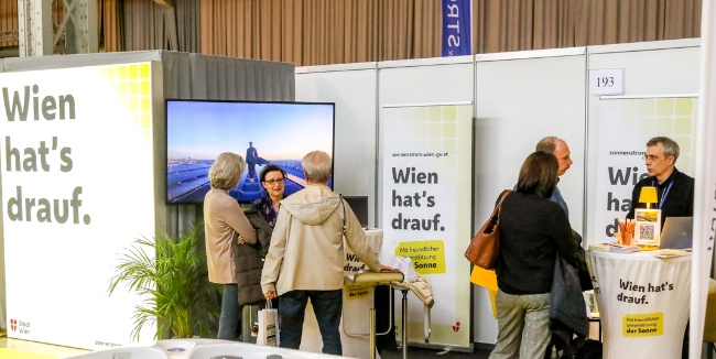 Messestand der Stadt Wien mit dem Slogan „Wien hat’s drauf“. Mehrere Personen führen Gespräche, im Hintergrund läuft auf einem Bildschirm ein Video über Sonnenstrom. Copyright: Stadt Wien/Christian Fürthner