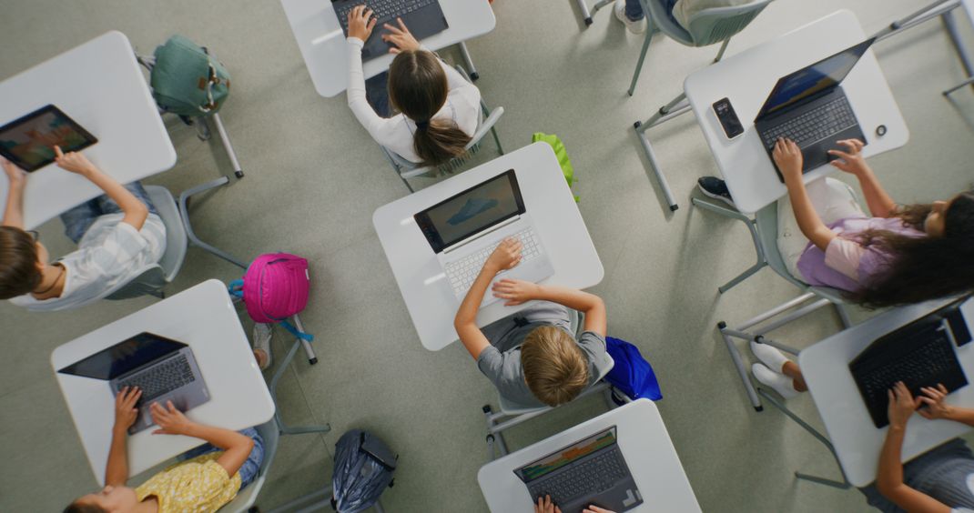 Vogelperspektive mehrere Tische mit Schüler*innen mit Laptops.
