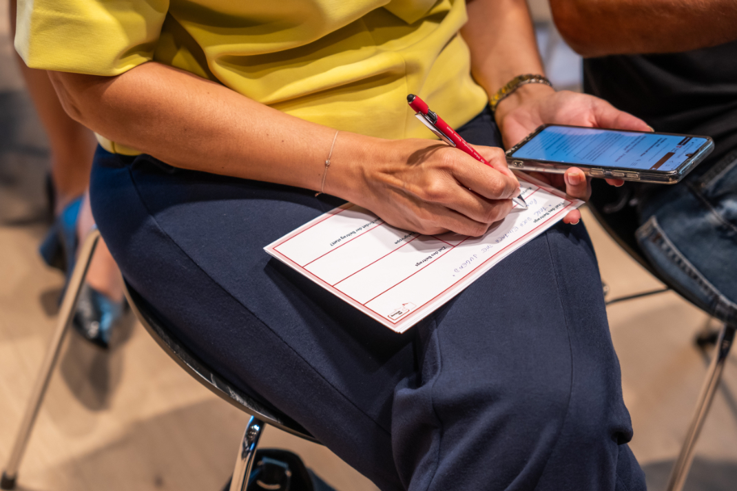 Kapitelbild: Eine Person auf einem Sessel schreibt mit einer Hand auf eine Karte und hält in der anderen ein Smarphone