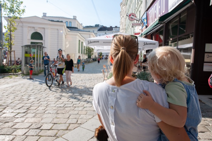 Mutter mit Kind auf dem Arm blickt eine Fußgängerzone entlang