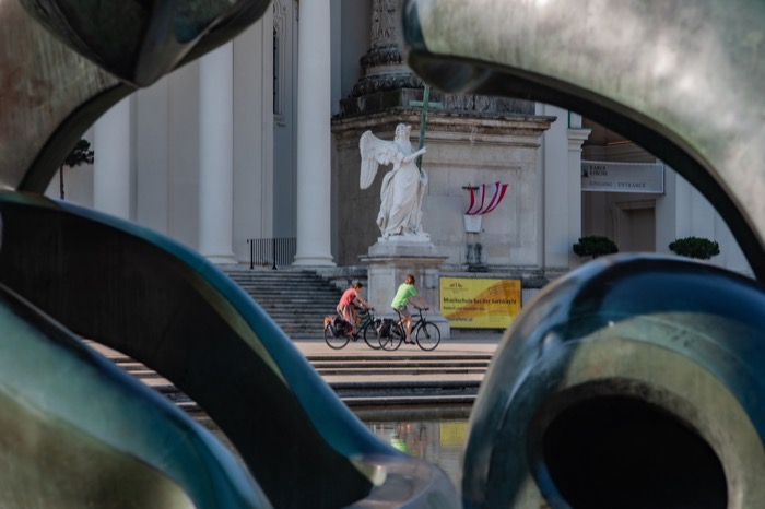 Zwei Radfahrer vor der Karlskirche mit Blick durch eine Statue