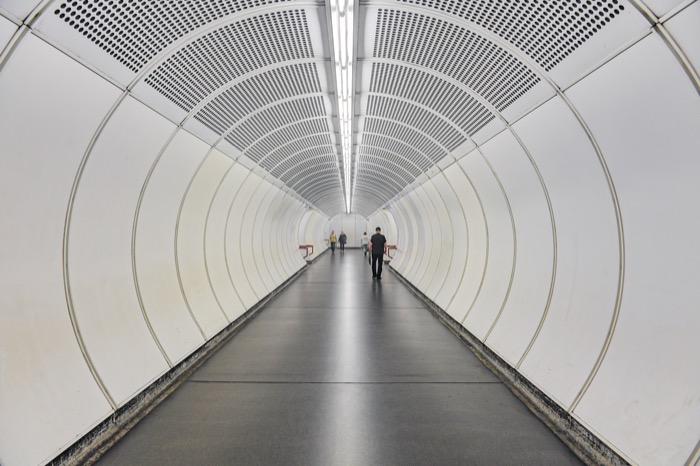 Personen gehen einen Gang mit abgerundeten Wänden in einer U-Bahn Station entlang