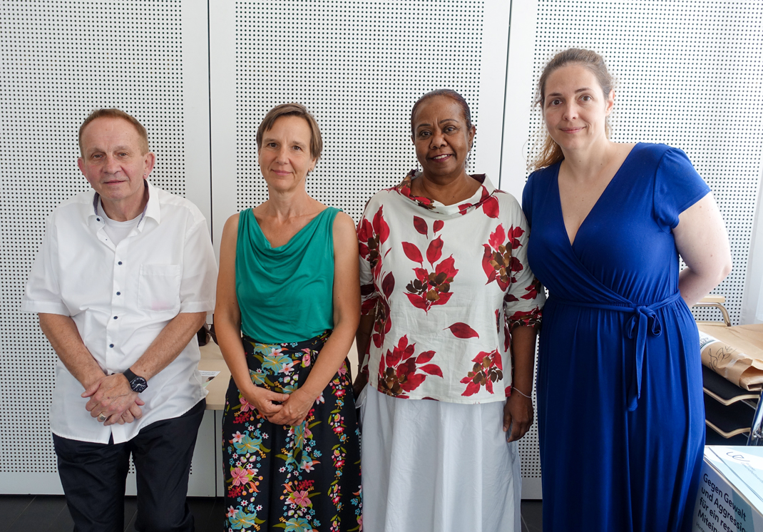 Zu sehen sind die vier Personen. Sie stehen Schulter an Schulter und blicken freundlich in die Kamera.