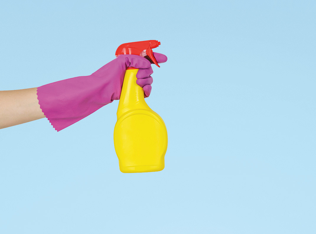 Eine Person tragt einen Putzhandschuh und hat eine Sprühflasche in der Hand.