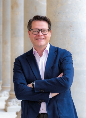 Formal portrait of City Councilor Jürgen Czernohorszky: He is wearing a blue blazer. There are columns in the background.