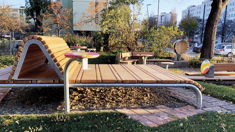 The photo shows a wave-shaped wooden platform on a steel tube frame with small round play tables.